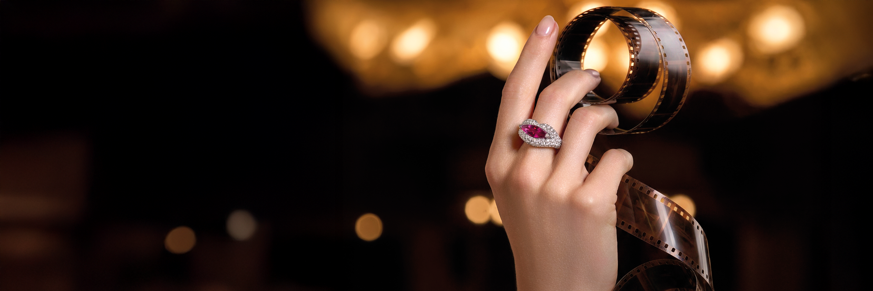 Ein mit Edelstein besetzter Ring ziert den Zeigefinger einer Dame. Es wird nur die Hand gezeigt, der Hintergrund ist in einem neutralen Farbton gehalten.