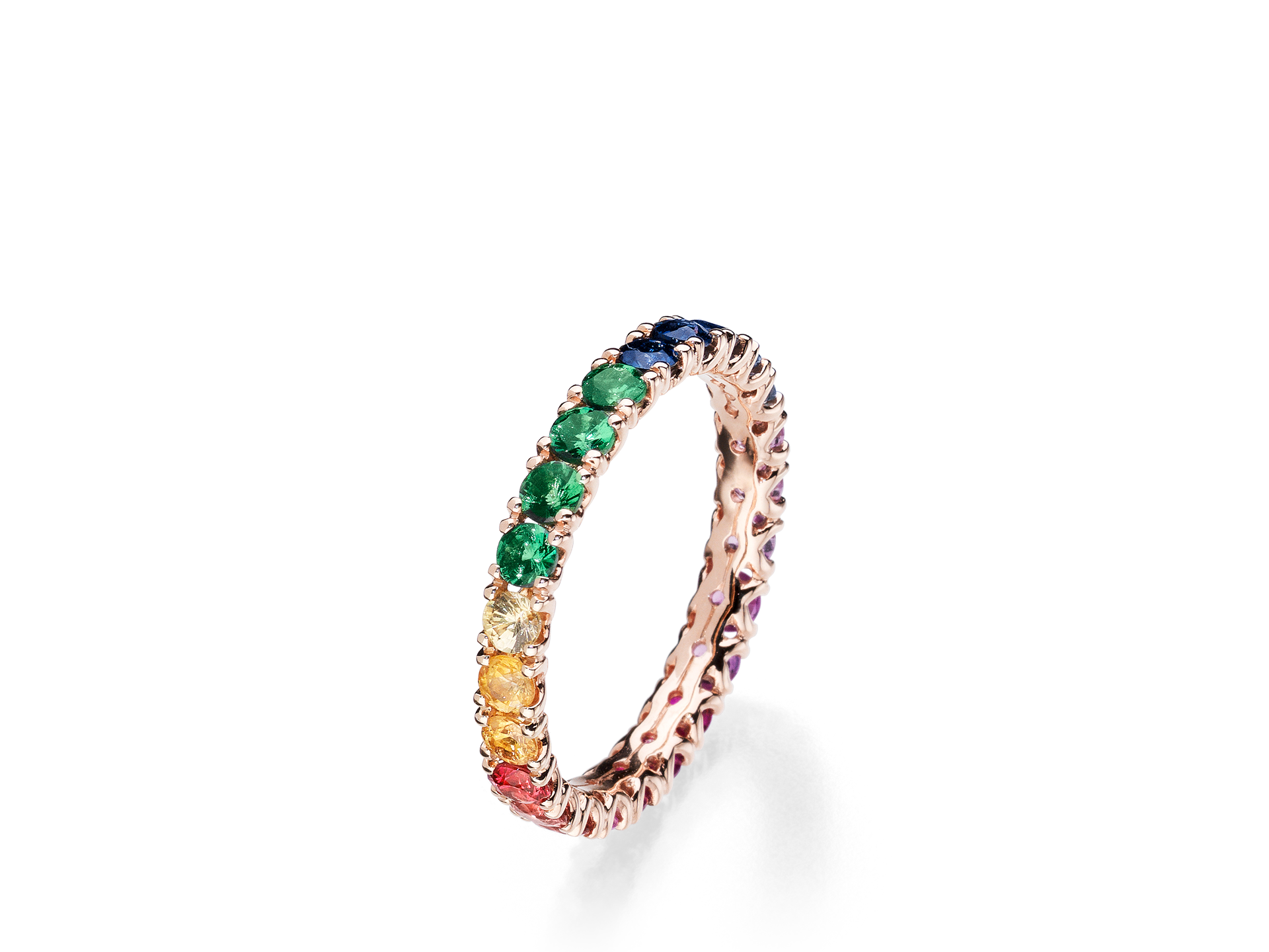 Der Schullin MEMOIRE RING RAINBOW ist ein schmales Goldband, das mit einer durchgehenden Reihe roter, gelber, grüner und blauer Edelsteine vor weißem Hintergrund verziert ist.