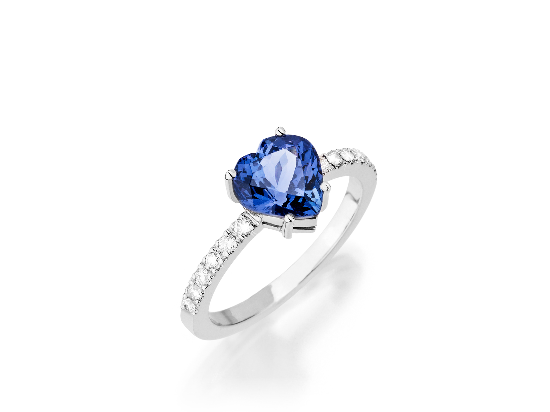 Der Schullin TANSANIT RING HEART zeigt einen herzförmigen blauen Tansanit in der Mitte, akzentuiert durch kleine runde weiße Diamanten auf dem Silberband, gefasst auf weißem Hintergrund.