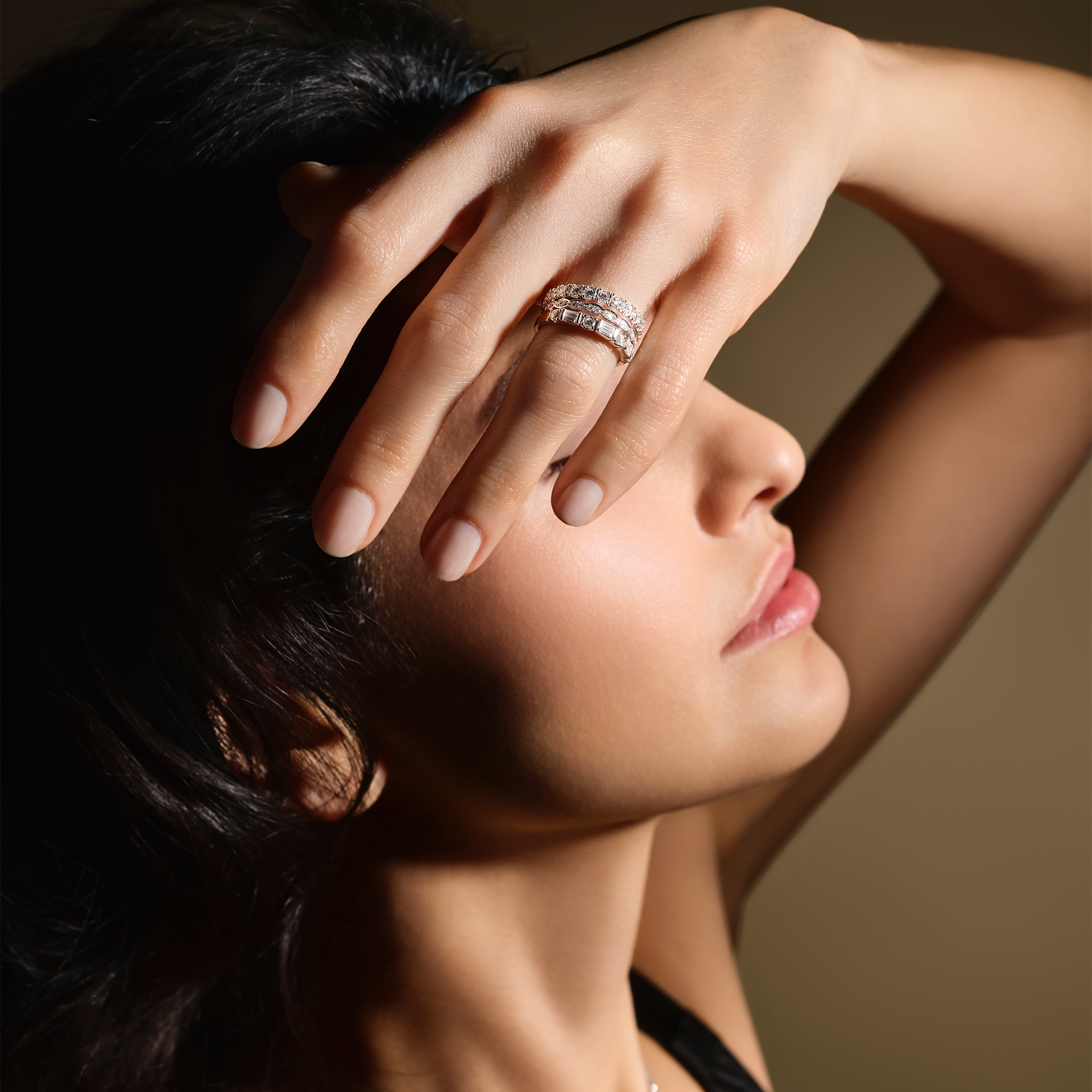 Eine Frau mit langen dunklen Haaren posiert im Profil unter sanfter Beleuchtung, die Hand erhoben, um den funkelnden Schullin DIAMANT RING an ihrem Finger zu präsentieren.