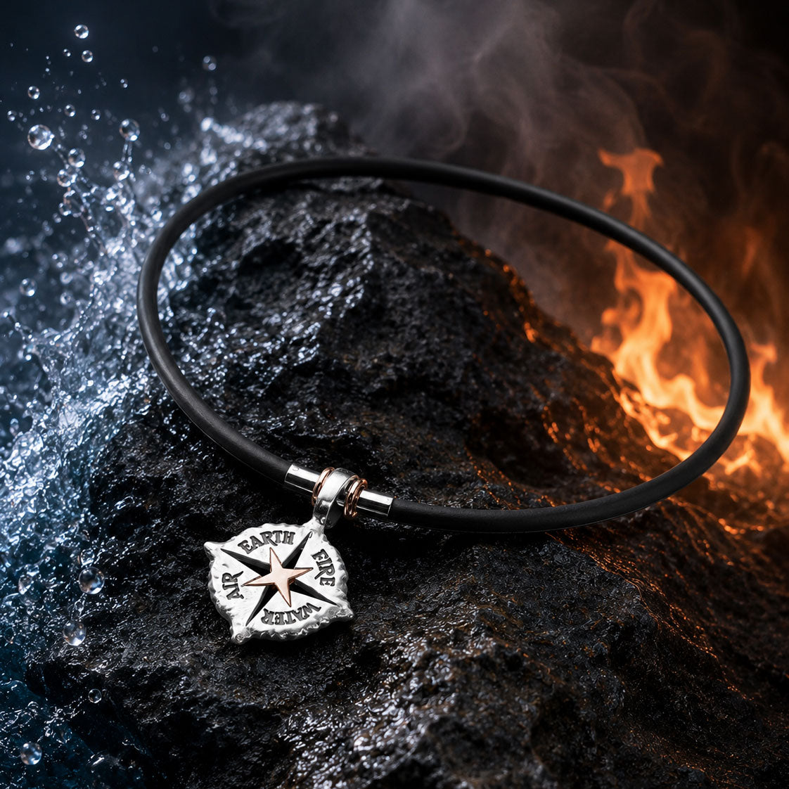 Die ELEMENTS KETTE STERLING SILBER von Schullin, eine schwarze Herrenkette mit einem sternförmigen Anhänger, auf dem Luft, Erde, Feuer und Wasser eingraviert sind, liegt auf dunklem Fels zwischen plätscherndem Wasser und hellen Flammen.
