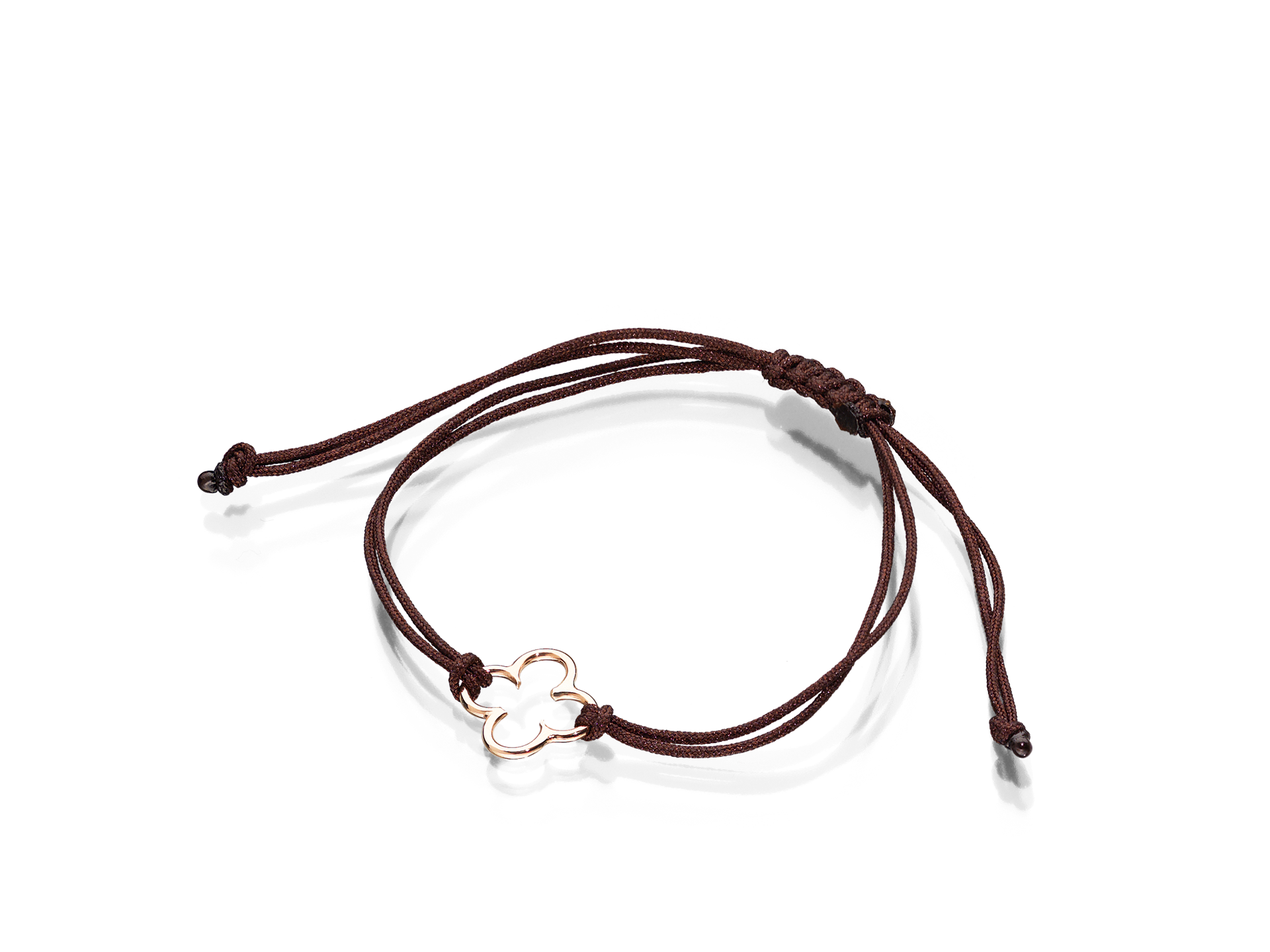 Das FLOWER ARMBAND von Schullin besteht aus einer dunkelbraunen Kordel mit verstellbarem Knoten und einem zentralen kleeblattförmigen Anhänger aus 18 Karat Roségold. Sein minimalistisches Design und die sanfte Farbpalette sorgen für einen schlichten und eleganten Look.