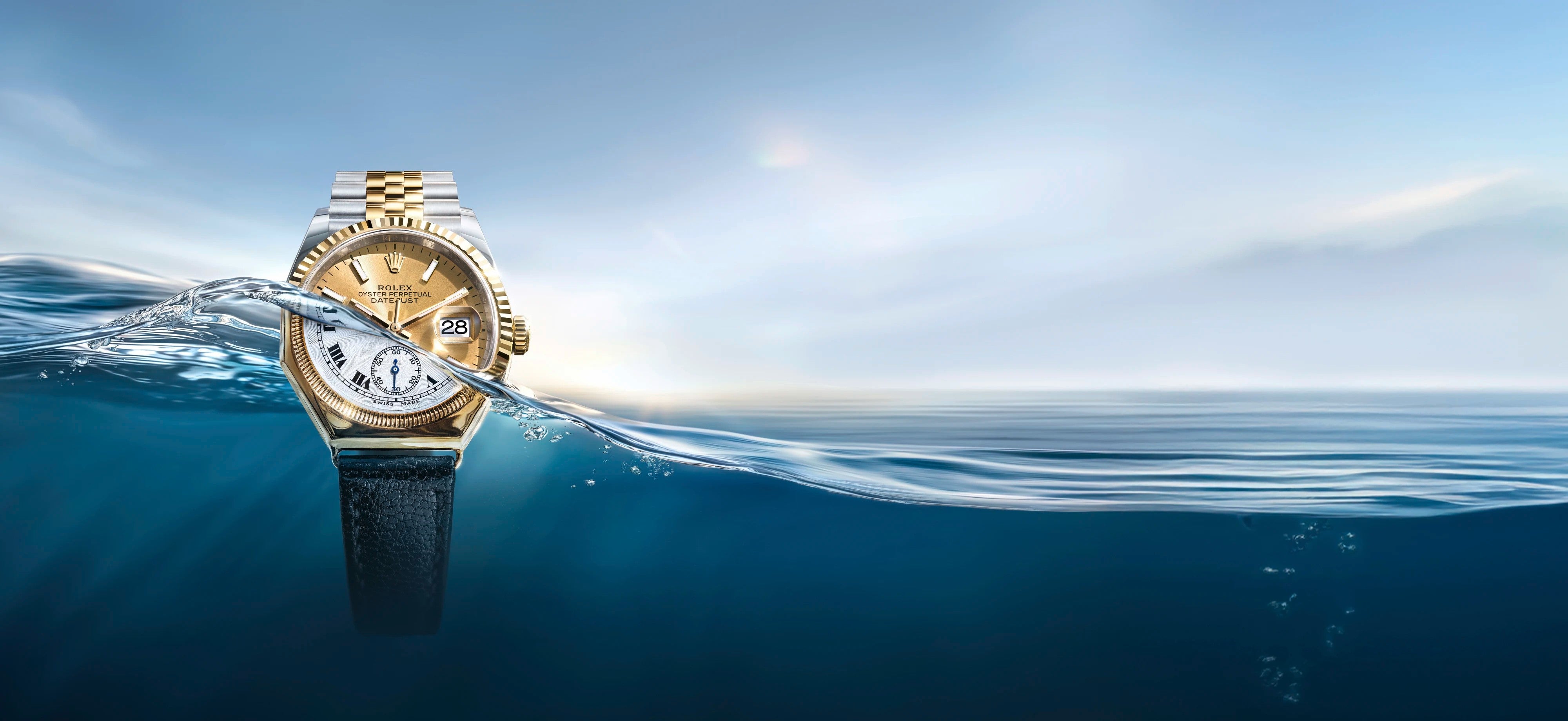 Eine luxuriöse Armbanduhr mit goldenem Zifferblatt und zweifarbigem Metallband ist teilweise in klares blaues Wasser getaucht, mit einem ruhigen Ozean und einem hellen Himmel im Hintergrund.