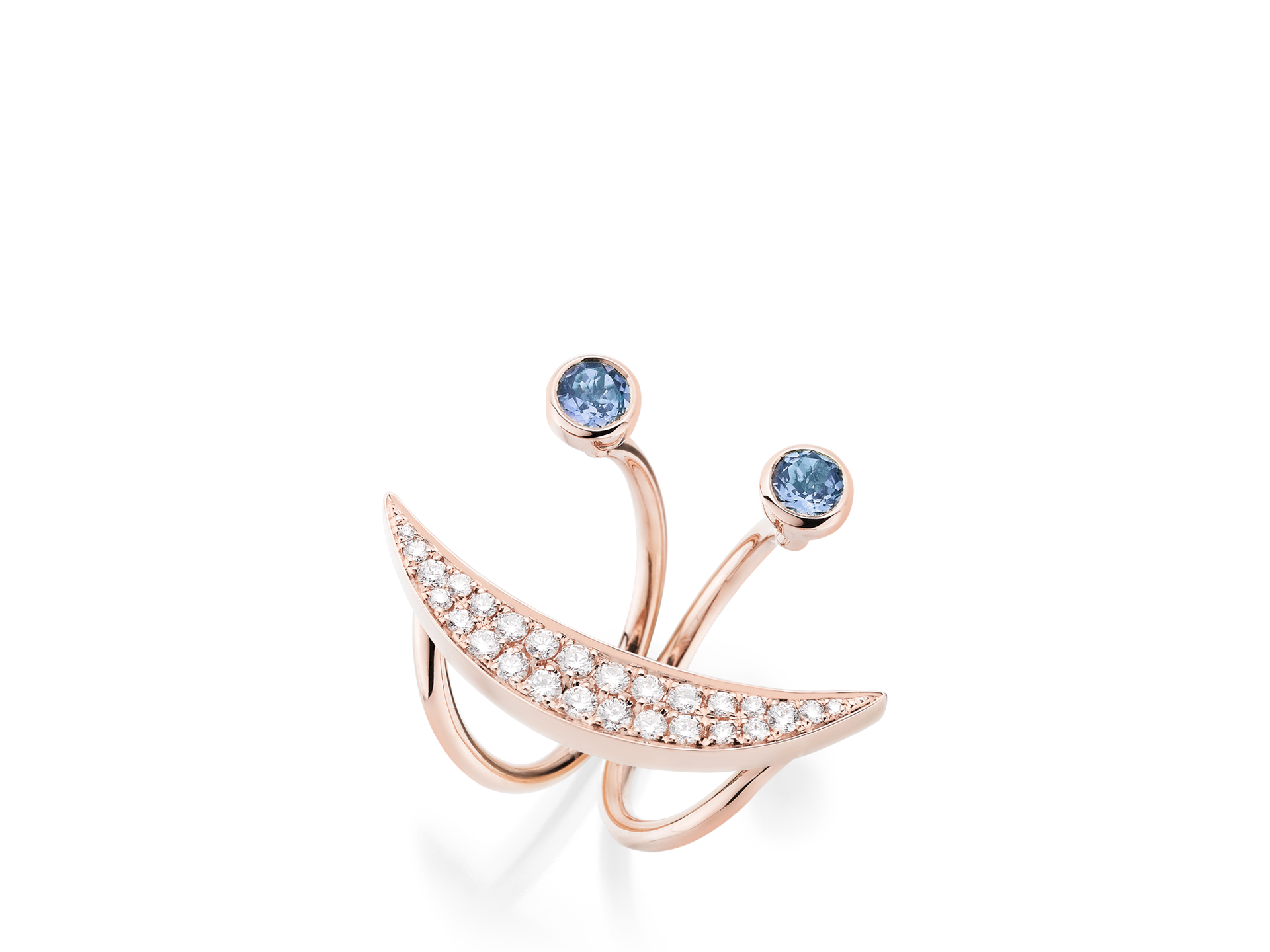 Der TANSANIT RING SMILE von Schullin besticht durch ein geschwungenes Design aus 18 Karat Roségold, das mit zwei blauen Tansaniten und einer Reihe kleiner weißer Diamanten verziert ist und ein atemberaubendes Diamant-Lächeln bildet. Ein anmutig offener Raum trennt die Mondsichel von den Edelsteinen.