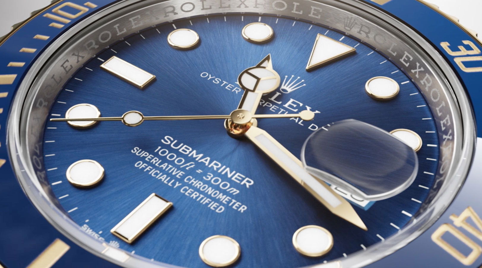 Nahaufnahme eines blauen Rolex Submariner-Zifferblatts mit goldenen Indexen und Zeigern, einem vergrößerten Datumsfenster und einer Oyster Perpetual Date mit Angaben zur Wasserdichtigkeit auf dem Zifferblatt.