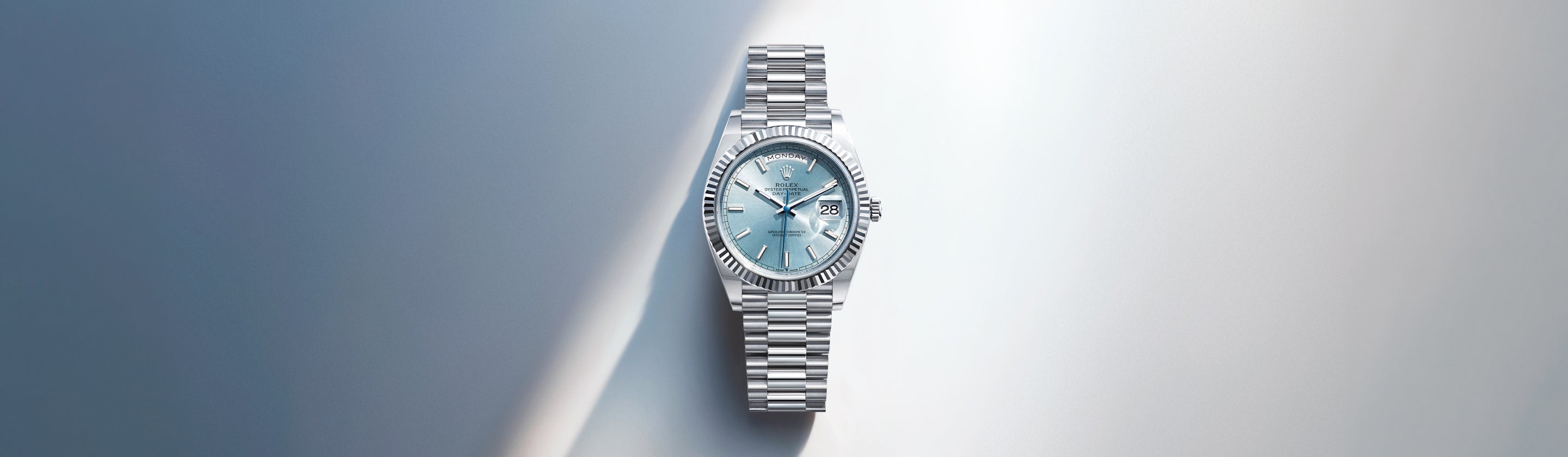 Eine silberne Armbanduhr mit hellblauem Ziffernblatt und Metallgliederband ist auf einem sanft beleuchteten Hintergrund mit Licht- und Schattenverläufen zentriert.