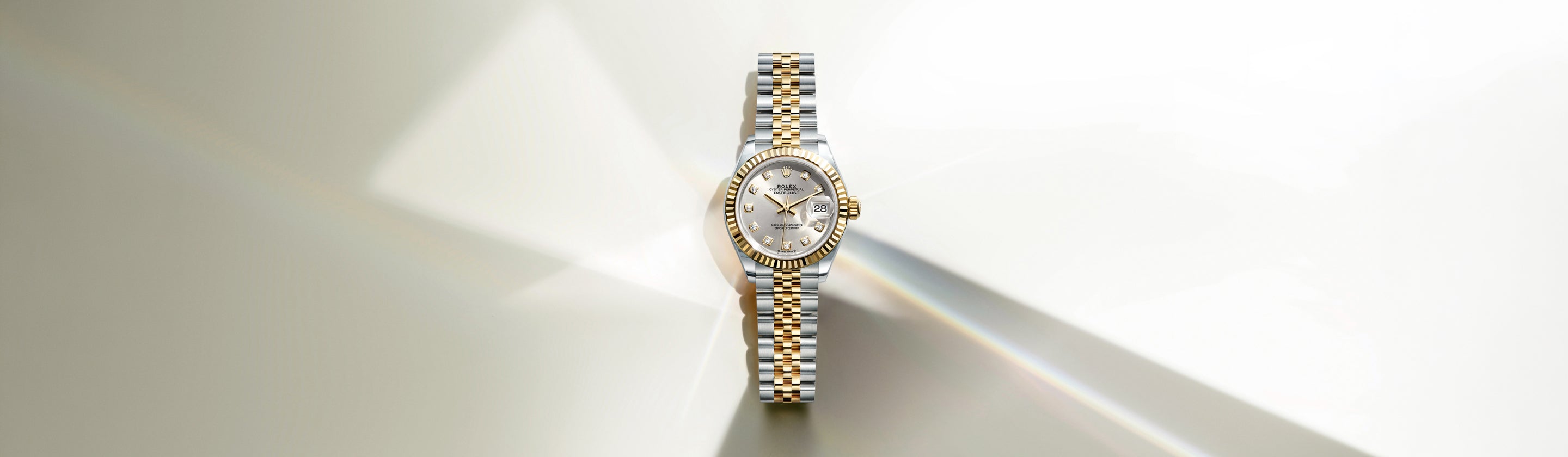 Eine luxuriöse Armbanduhr aus Silber und Gold mit Diamantlünette und -armband, dargestellt auf einem hellen Hintergrund mit weichen Reflexen und Schatten.