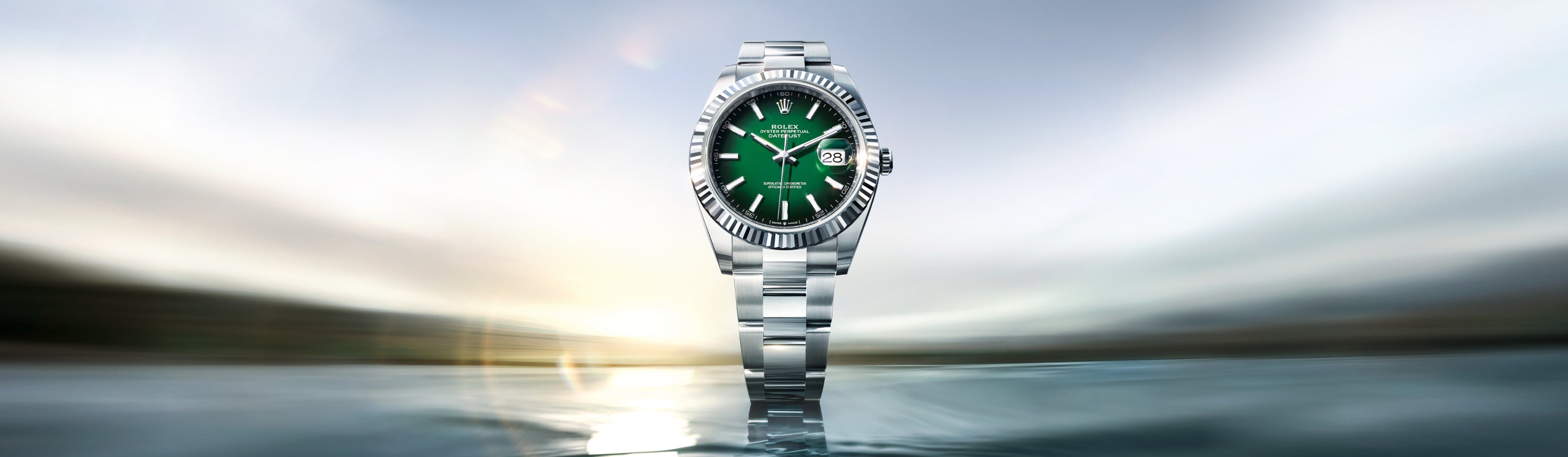 Eine silberne Rolex-Armbanduhr mit grünem Zifferblatt und Datumsanzeige ist vor einem unscharfen, hellen Hintergrund zentriert, wodurch ein dynamischer und luxuriöser Effekt entsteht.