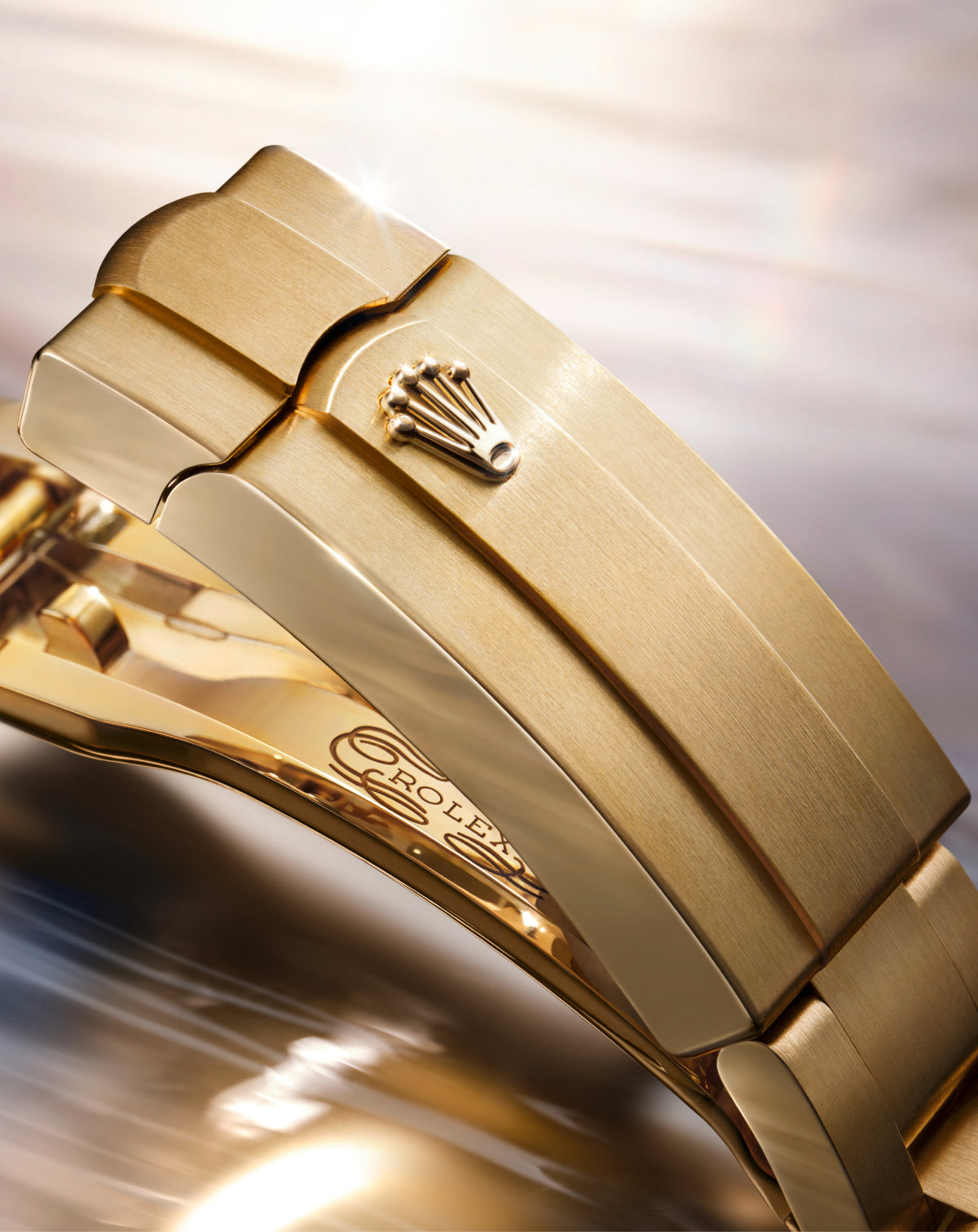 Nahaufnahme einer goldenen Rolex-Uhrenschließe mit dem eingravierten Rolex-Kronenlogo auf der gebürsteten Metalloberfläche, mit weichen Lichtreflexen im Hintergrund.