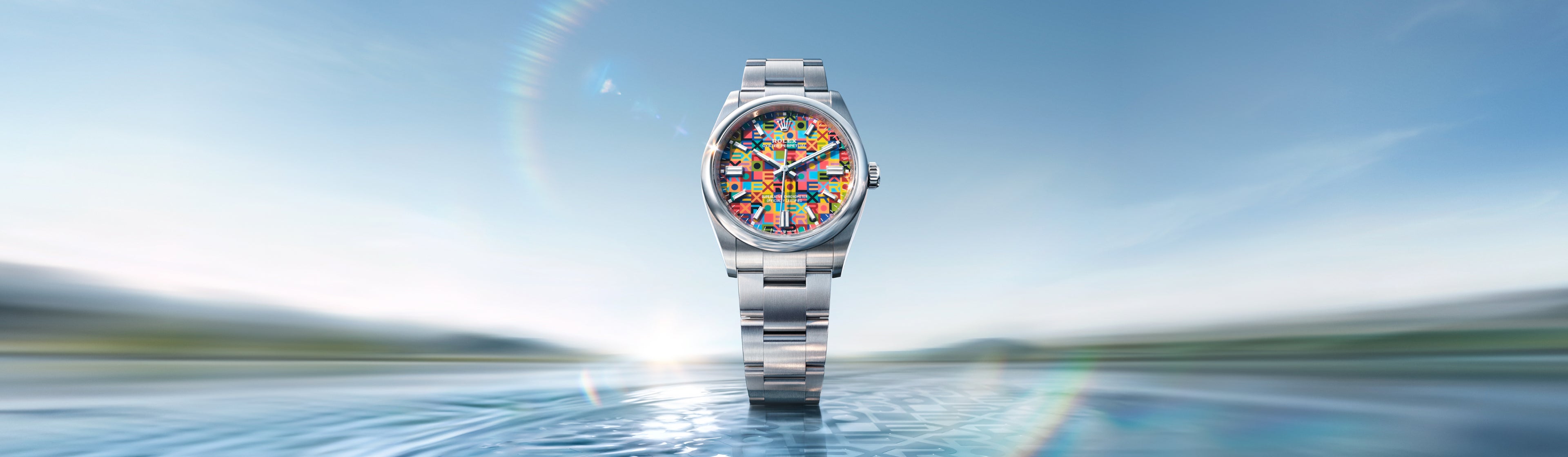 Eine silberne Armbanduhr mit einem farbenfrohen, abstrakten Mosaikzifferblatt ist vor einem unscharfen blauen und grünen Hintergrund zentriert, was der Uhr ein Gefühl von Bewegung und Fokus verleiht.
