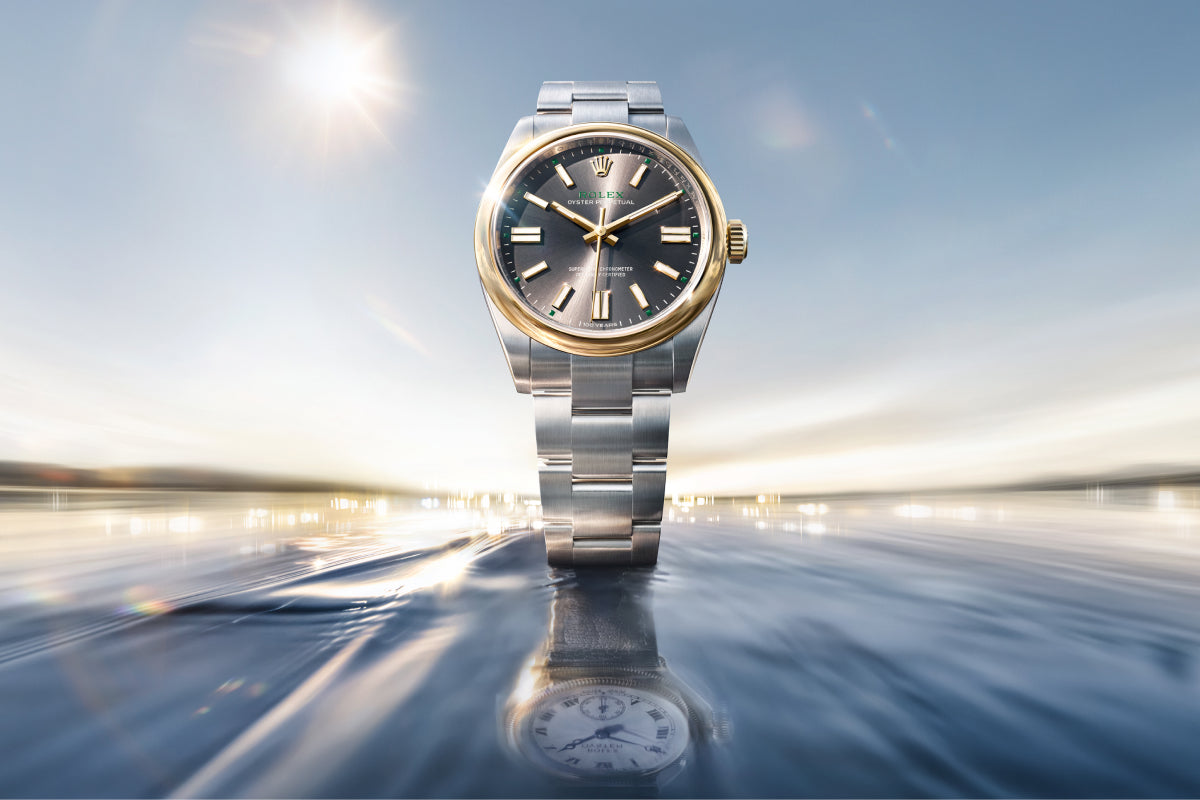 Eine luxuriöse Armbanduhr mit silbernem Band und goldener Lünette steht aufrecht auf einer spiegelnden, gewellten Oberfläche, mit ihrem Spiegelbild darunter und einem hellen, verschwommenen Himmel im Hintergrund.