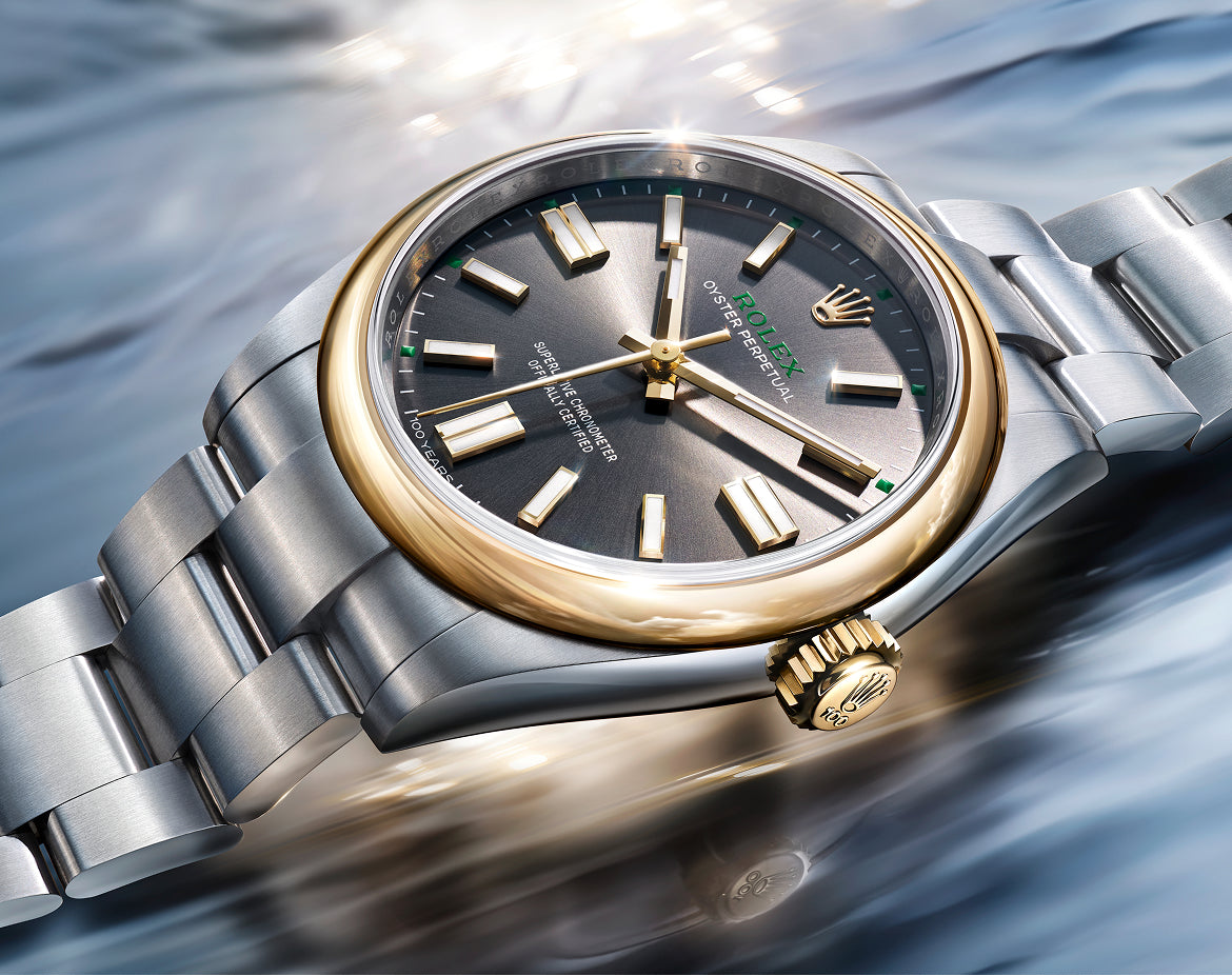 Nahaufnahme einer luxuriösen Armbanduhr mit goldener Lünette, dunklem Zifferblatt und silbernem und goldenem Metallarmband, die auf einer reflektierenden, gewellten Oberfläche mit schimmernden Lichtreflexen ruht.