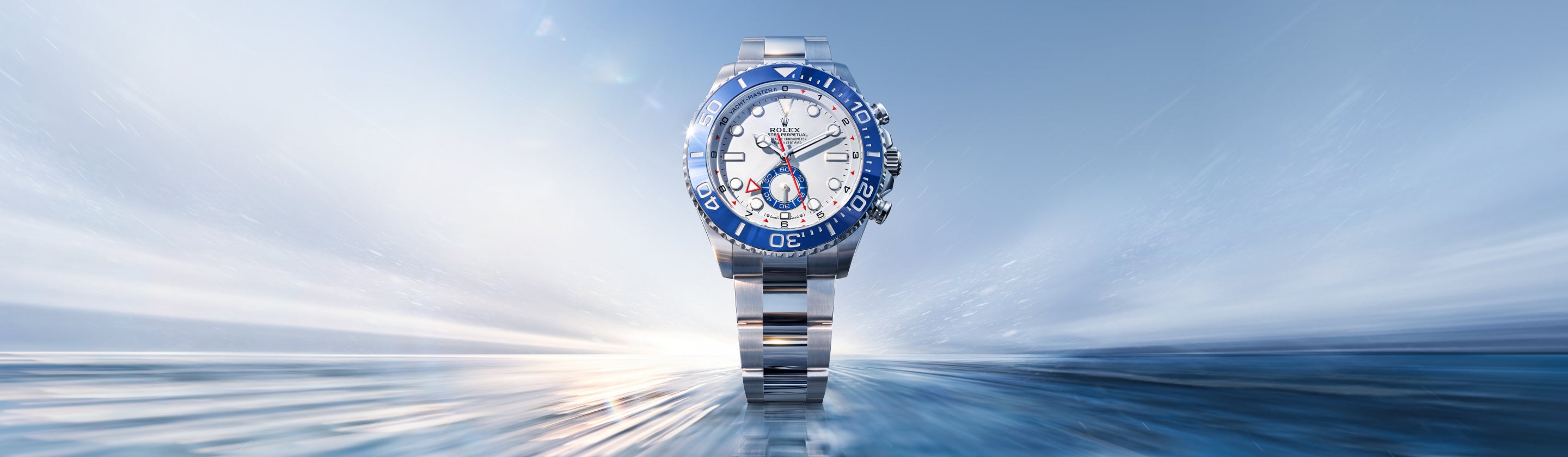 Eine silberne Rolex Yacht-Master II Uhr mit blau-weißem Zifferblatt wird vor einem verschwommenen blau-weißen Hintergrund zentriert, wodurch ein eleganter und dynamischer visueller Effekt entsteht.