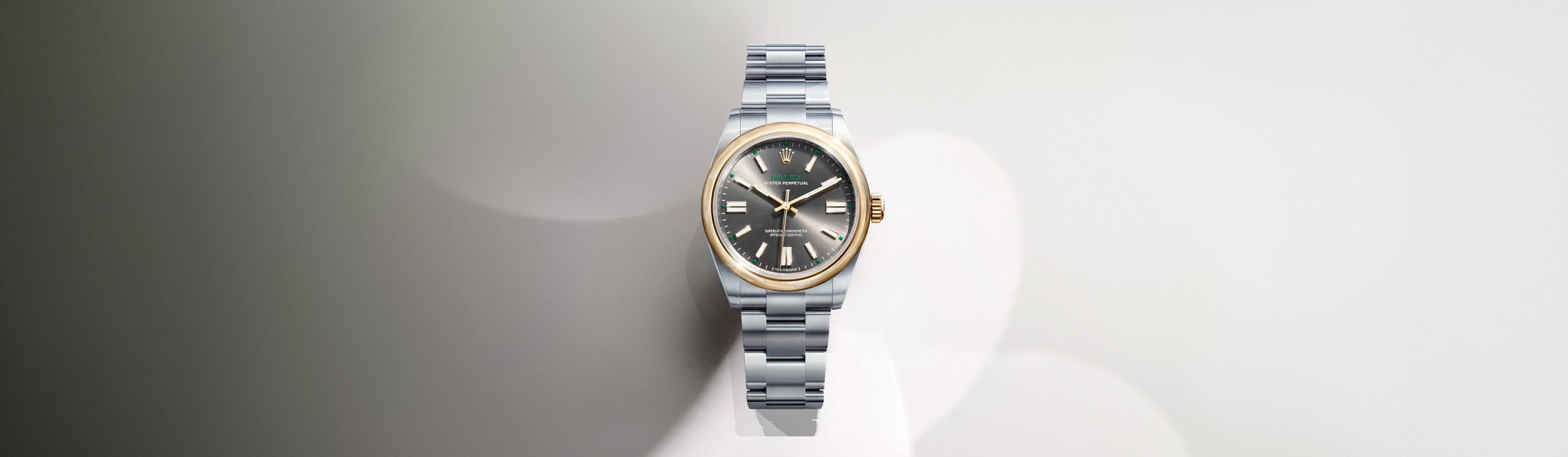 Eine luxuriöse silberne Armbanduhr mit metallischem Gliederband, schwarzem Zifferblatt, goldener Lünette und goldenen Indexen vor einem sanft verschwommenen, hellgrauen Hintergrund.