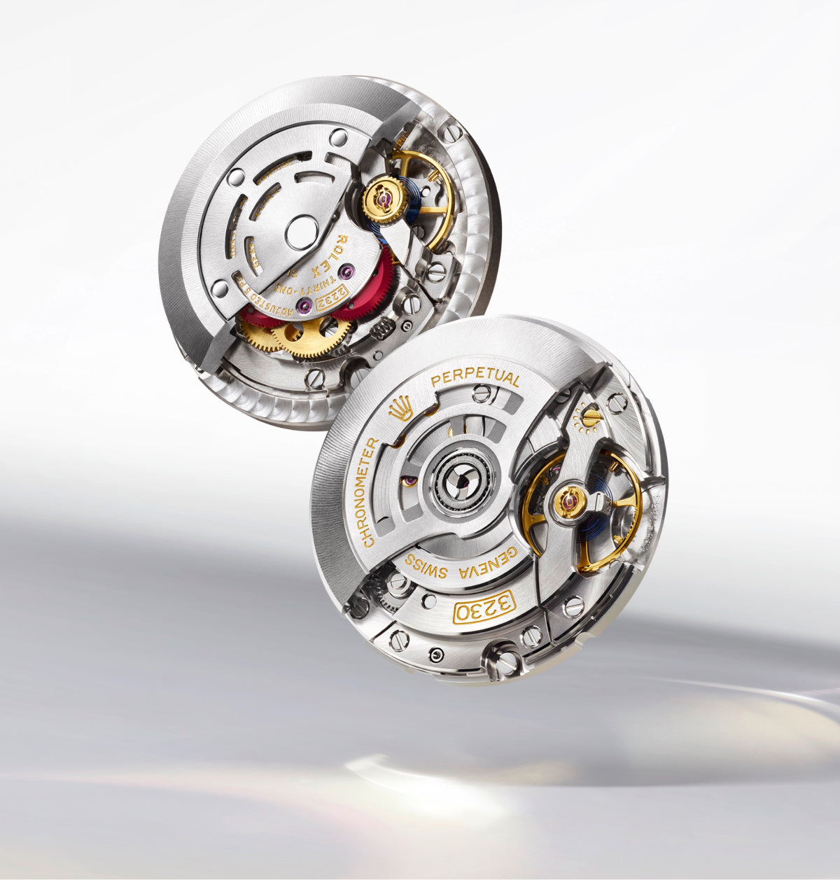 Zwei komplizierte, metallische Schweizer Uhrwerke mit sichtbaren Zahnrädern, Schrauben und Goldgravuren, darunter die Worte PERPETUAL und CHRONOMETER, die auf einer hellen, reflektierenden Oberfläche angebracht sind.