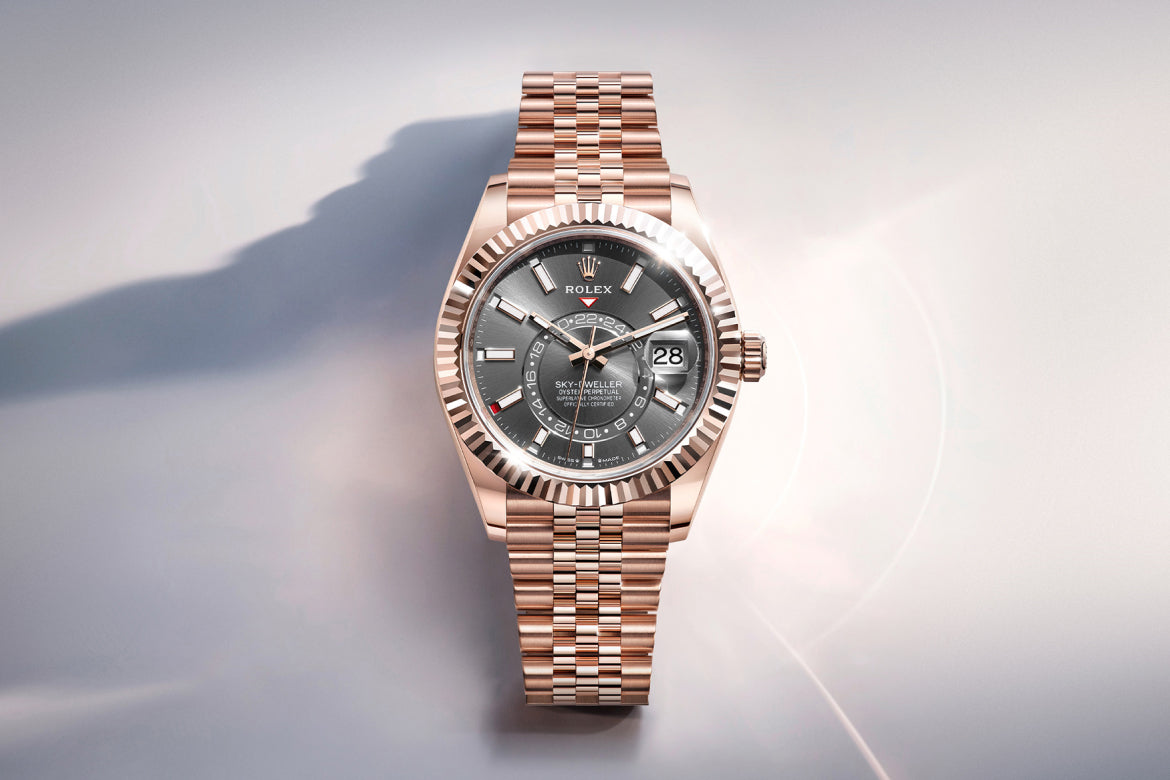 Eine roségoldene Rolex-Armbanduhr mit kannelierter Lünette und grauem Zifferblatt mit Datumsfenster und verschlungenen Hilfszifferblättern wird auf einer hellen Oberfläche mit weichen Schatten präsentiert.